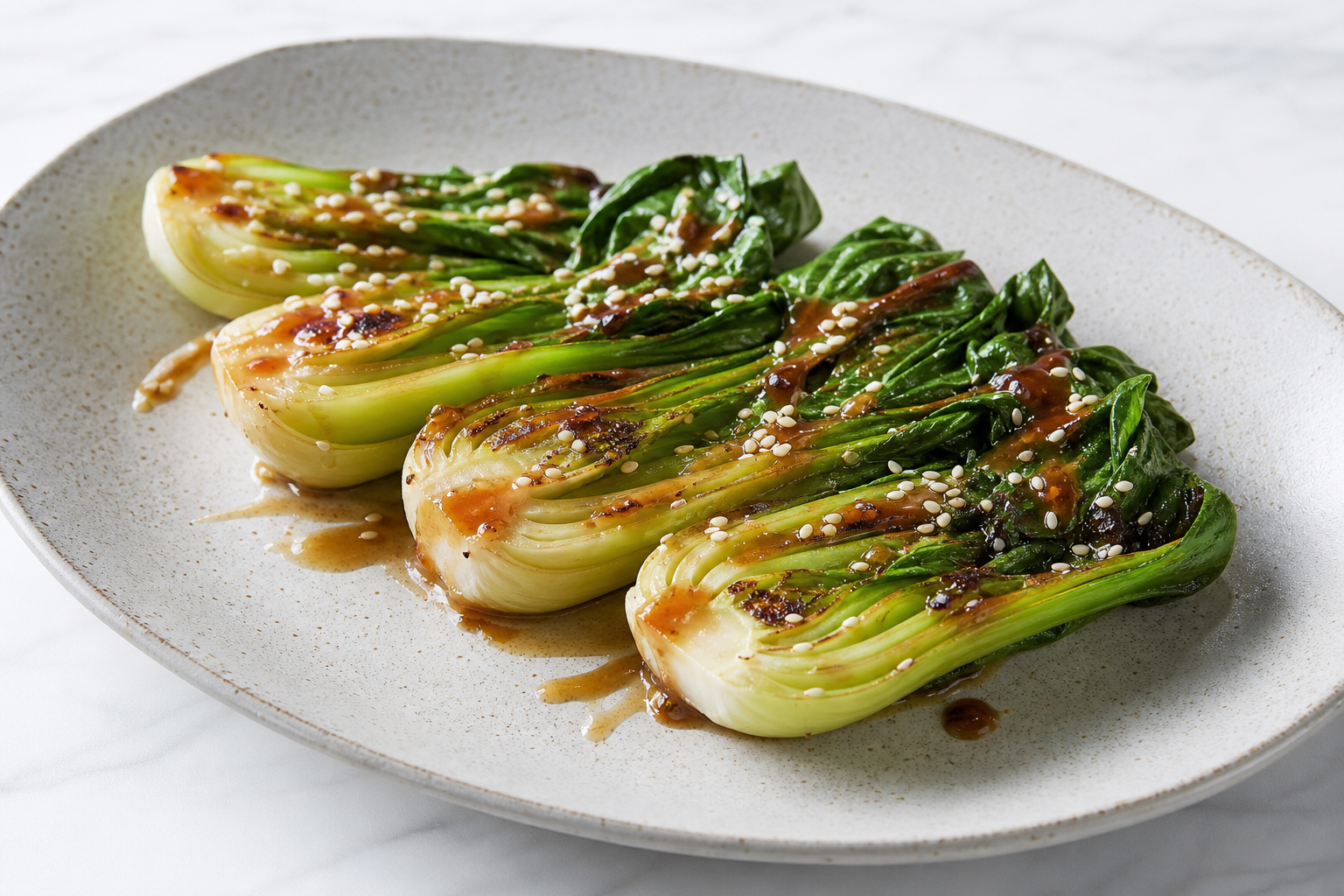 Halveret pak choi på fad med sesam og mørk misoglaze på tallerken